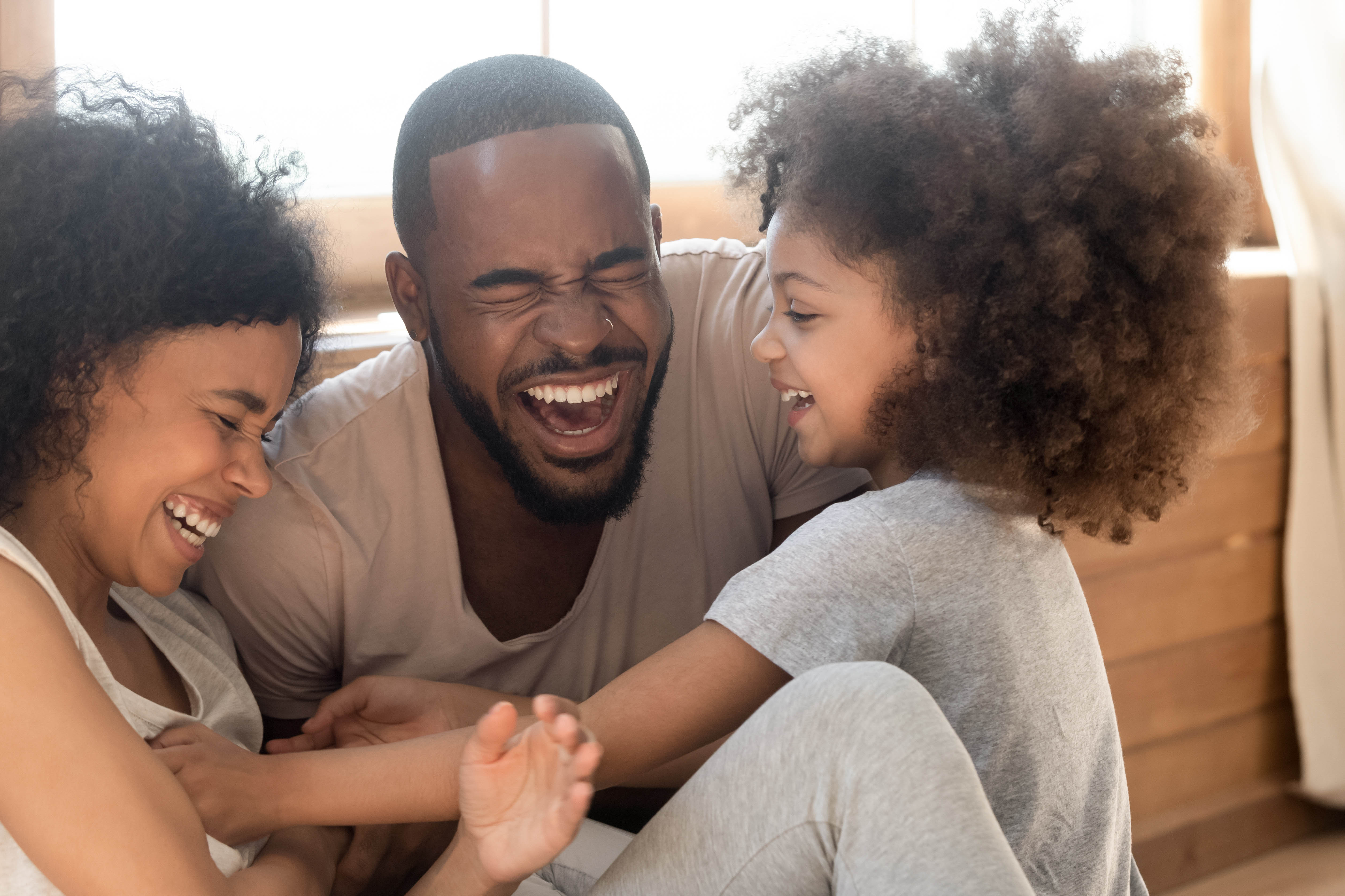 Happy mom, dad, and young girl sitting on the floor laughing together